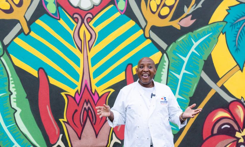 Glen from Glen's Kitchen standing in front of a brightly coloured garfitti mural, he is smiling with his hands out stretched palms up
