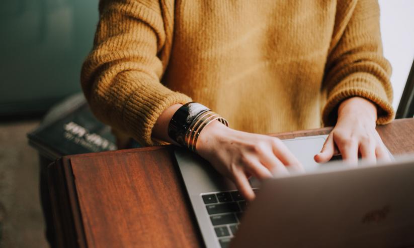 Person (face not visable) wearing a yellow jumper and a watch on their wrist working on a laptop