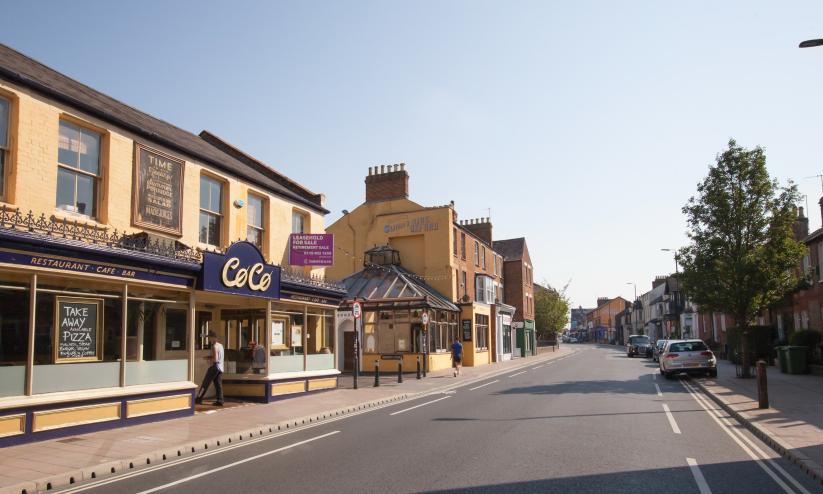 A view of a sunny street with cafes and a tree, this is Cowley Road in Oxford